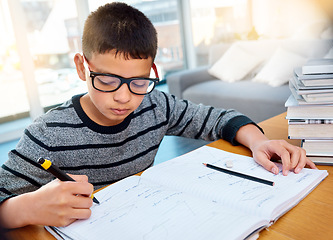 Image showing Boy child, student and writing in book for studying, education and learning homework on table at home. Smart little kid busy with mathematics, textbooks and problem solving for study in living room