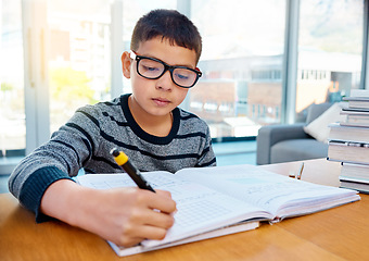 Image showing Boy, student and writing in book for studying, homework or learning in education on table at home. Smart little kid or child busy on mathematics, textbooks or problem solving for study in living room