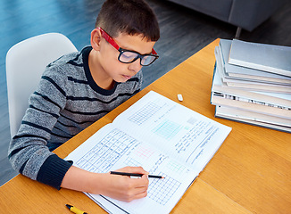 Image showing Boy, student and writing in book for math, studying or homework for learning, assessment or education on table. Smart kid, young child and busy reading mathematics textbook, problem solving and focus