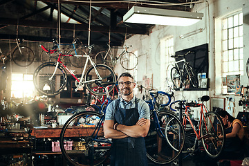 Image showing Happy, portrait and repair man in bicycle shop with arms crossed in small business workshop. Owner, bike mechanic and smile of confident person, professional or mature technician and glasses in store