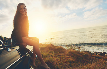 Image showing Road trip, portrait and sunset with a woman at the ocean, sitting on her car bonnet during travel for freedom or escape. Nature, flare and mockup with a young female tourist traveling in summer