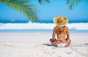 Image showing Relax, back view of a woman on the beach and sitting on the sand, Summer vacation or holiday break, freedom or adventure and female person relaxing at the sea with blue sky for peace in nature