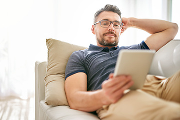 Image showing Tablet, relax and man on a sofa in the living room watching a video on social media or the internet. Rest, browsing and mature male person reading an online blog on digital technology at his home.