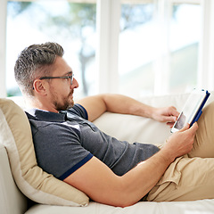 Image showing Man, relax and tablet on living room sofa, reading and social media for video, game or movies in home. Mature guy, digital touchscreen and lounge couch for internet blog, news and web app in house