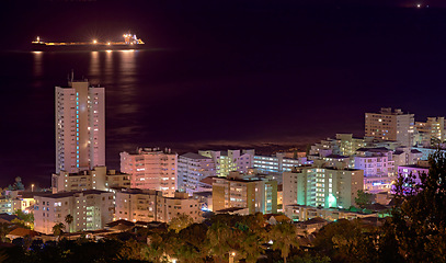 Image showing Lights, buildings and city at night with a harbour for urban development, sea water and streets. Dark, travel and aerial view of outdoor residential architecture of downtown with an ocean in evening.