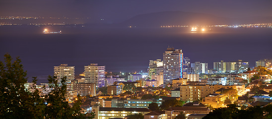 Image showing Harbour, buildings and city at night with lights, urban development and streets. Dark, travel and outdoor residential architecture of downtown with ocean or sea water in the evening with a skyline.