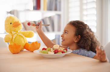 Image showing Child feeding, teddy bear and food at home with happiness and wellness meal with a smile. House, nutrition and young girl with healthy fruit salad and fruits of a hungry kid with toy duck at a table