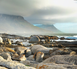 Image showing Sea, rocks and landscape with beach and travel destination, waves and summer vacation in Cape Town. Environment, ocean view and seaside location with mountain and clouds, nature and adventure outdoor