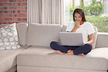 Image showing Laptop, eating apple and a woman on a home sofa with internet for streaming, remote work and reading blog online. Happy female person relax on couch with fruit, snack and computer for elearning tech