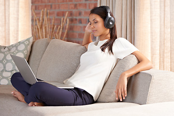 Image showing Laptop, headphones and woman on a home sofa listening to music or streaming movies online. Calm female person relax on couch to listen to radio or video with internet connection and technology