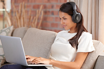 Image showing Headphones, home and a woman typing on laptop on home sofa listening to music or streaming movies. Calm female person relax on couch to listen to radio or learning a language with internet connection