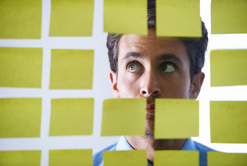 Image showing Creative man, face and thinking in sticky note for schedule brainstorming or planning tasks on glass board at office. Male in doubt, decision or problem solving for startup idea strategy at workplace