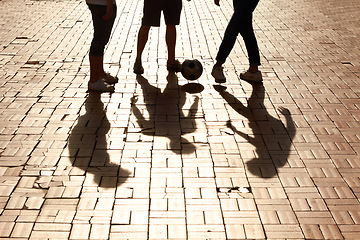 Image showing Sports, football and shadow of friends with a ball training for a skill, trick or stunt on a pavement. Silhouette, soccer and legs of people practicing for a game, match or tournament in the city.