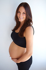 Image showing Woman, pregnancy portrait and stomach by wall with smile, excited or pride for new life, future or family. Young mom, pregnant and holding belly with happiness, love or care in house with expectation