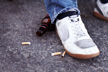 Image showing Feet, cigarettes and beer in a road in the city for a man with sneakers smoking and drinking. Shoes, addiction and closeup of tobacco and an alcohol bottle in the outdoor street of an urban town.