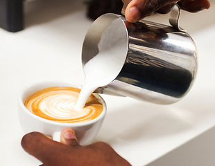 Image showing Coffee, closeup hand of a barista and pouring milk in a cup in a cafe in the morning. Latte or cappuccino, cafeteria and hands of a person pour a hot beverage for expresso drink at kitchen counter