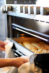 Image showing Hands, closeup and tray from oven for bread, baking product or food for small business, cafe or restaurant. Chef, baker or person with cloth for safety in bakery, coffee shop or food industry startup