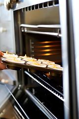 Image showing Hands, closeup and tray in oven for cupcake, baking and food for small business, cafe or restaurant. Professional chef, baker or person with muffin in bakery, coffee shop or food industry startup