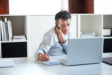 Image showing Consultant, businessman with smartphone on a call and with laptop writing notes in a notebook at his office. Customer service or online communication, networking and male person a cellphone at desk