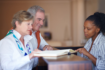 Image showing Booking, receptionist desk and couple for check in, hospitality and tourism vacation or holiday services. Mature people, woman or concierge writing, sign and hotel registration, advice or information