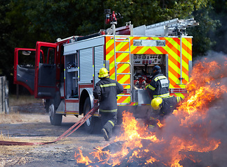 Image showing Fire, teamwork and truck with firefighter and emergency in nature for smoke, safety and explosion. Danger, fearless and training with team of men in outdoor for rescue, saving operation and action