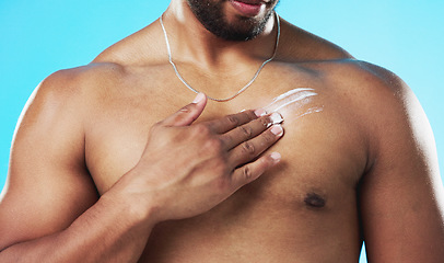 Image showing Skincare, applying and man with cream on his chest isolated on a blue background in a studio. Moisturizing, sexy and male model with sunscreen, lotion or moisturizer on his body for grooming