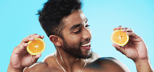 Image showing Orange, skincare and face of man in studio for beauty, wellness and citrus treatment on blue background. Fruit, facial and portrait of indian male model excited for organic vitamin c skin cosmetics