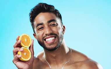 Image showing Happy, orange and face of man in studio for skincare, wellness and citrus treatment on blue background. Fruit, facial and portrait of indian male model excited for organic vitamin c skin cosmetics