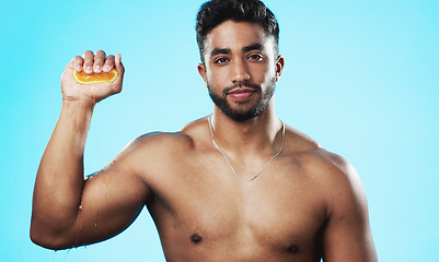 Image showing Skincare, squeeze and face of man with orange in studio for beauty, wellness and citrus treatment on blue background. Fruit, facial and portrait of indian guy model with organic, anti aging vitamin c