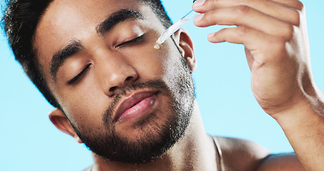 Image showing Skincare, health and man with face serum in a studio with a beauty, grooming and face routine. Wellness, cosmetic and male model with a facial oil pipette for a skin treatment by a blue background.