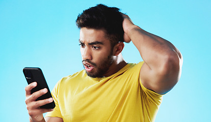 Image showing Phone, wow or bad news with a man reading a negative text message in studio on a blue background. Mobile, contact and surprise with a young male looking shocked by a social media post or announcement