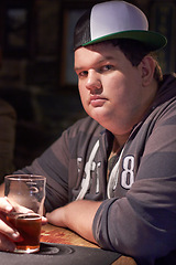 Image showing Man portrait, pub beer and plus size person waiting for a alcohol and drink looking serious. Male person, restaurant and glass pint sitting at a counter at a club with gen z, cool and urban fashion