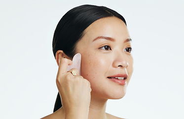 Image showing Gua sha, beauty and woman massaging face isolated on a white background in a studio. Spa, skincare and an Asian girl with a product to massage for facial relaxation, treatment and anti aging