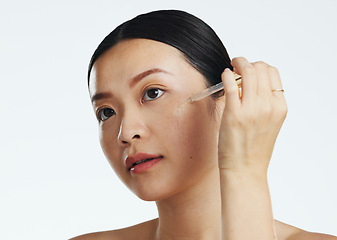 Image showing Asian woman, dropper and keratin on face for beauty, skincare or cosmetics against white studio background. Happy female model applying oil drop to skin for hydration, moisturizer or facial treatment