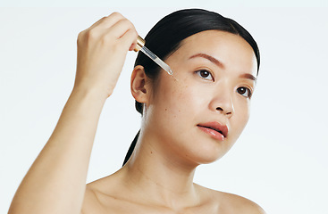 Image showing Asian woman, face and oil serum for beauty, facial skincare or dropper of hyaluronic acid in studio. Female model, cosmetics product and liquid collagen of glow, shine or thinking on white background