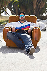 Image showing Portrait, man with sunglasses and street or urban, fashion and relax with cool streetwear style in the city. Person, face and stylish model with cap relaxing, chair or outdoor couch and sofa