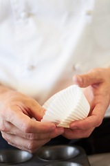 Image showing Cupcake, person hands and baking in a kitchen with muffin wrapper and cooking in a bakery. Prepare, paper cup and food with chef in a restaurant, coffee shop or cafe with sweet cake and pastry