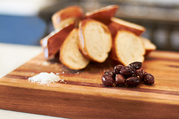 Image showing Olives, food and bakery with bread in kitchen for nutrition, health and diet. Breakfast, cafe and coffee shop with closeup of product on cutting board on table for wheat, grain and cooking