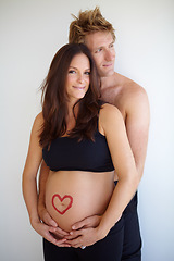 Image showing Pregnant, hug and portrait of couple with heart on stomach for love, care and support on white background. Family, pregnancy and man and woman in studio excited for baby with love symbol on belly