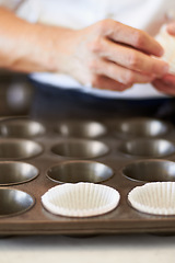 Image showing Cupcake tray, person hands and baking in kitchen with muffin wrapper and cooking closeup in bakery. Prepare, paper cup and food with chef in restaurant, coffee shop or cafe with sweet cake or pastry