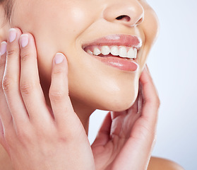 Image showing Skincare, smile and hands on face of woman in studio for healthy skin, glow or treatment on blue background. Happy, beauty and mouth of lady model with luxury hydration cosmetics, lip gloss or makeup