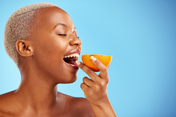 Image showing Orange, skincare and nutrition with a model black woman in studio on a blue background biting fruit. Food, beauty and natural with a happy young female person eating a snack for health or wellness