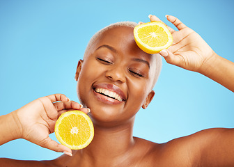 Image showing Orange, face and nutrition with a model black woman in studio on a blue background for treatment. Beauty, skincare and smile with a happy young person holding natural fruit for health or wellness