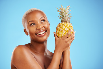 Image showing Happy black woman, pineapple and thinking for diet or natural nutrition against a blue studio background. Thoughtful African female person in wonder with organic fruit for vitamin, fiber or wellness