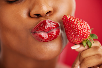 Image showing Kiss, beauty and woman with strawberry on face with skincare or lips in red background or closeup. Cosmetics, wellness and nutrition with female or fruit in studio for detox and diet or self love.