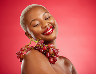 Image showing Skincare, smile and grapes with a model black woman in studio on a red background for health or nutrition. Beauty, happy and fruit with a young female person posing for wellness, diet or detox