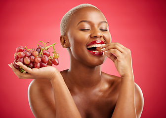 Image showing Health, eating and a black woman with grapes on a red background for nutrition or diet. Smile, beauty and an African model or girl with fruit, hungry and food for a detox isolated on a backdrop