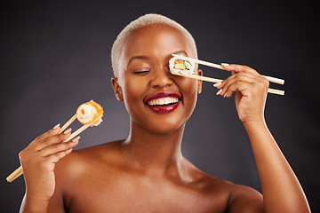 Image showing Sushi, face and woman with chopsticks in studio for healthy eating, beauty glow and food. Black female aesthetic model with makeup on a dark background for wellness, funny diet or seafood advertising