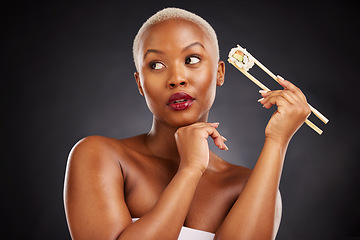 Image showing Face, thinking and woman with sushi and chopsticks in studio for healthy eating, beauty or food. Black female model with makeup idea on dark background for wellness glow, diet or seafood advertising