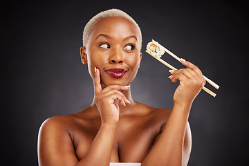 Image showing Sushi, thinking and face of a woman with chopsticks in studio for healthy eating, beauty or food. Black female model with makeup on dark background for wellness glow, diet or seafood advertising idea